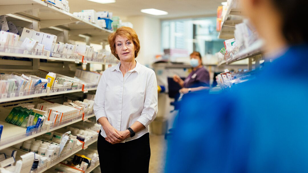 A woman stands in a pharmacy store, surrounded by shelves of health products and medications.